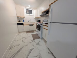 Eine kleine Küche mit weißen Schränken, einem Backofen, einer Mikrowelle und einem Kühlschrank.