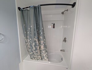 A shower with a curved showerhead, a bathtub, and a shower curtain with a floral pattern.
