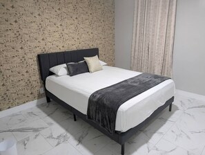 Ein Bett mit dunklem Kopfteil, weißer Bettwäsche und einer grauen Decke.