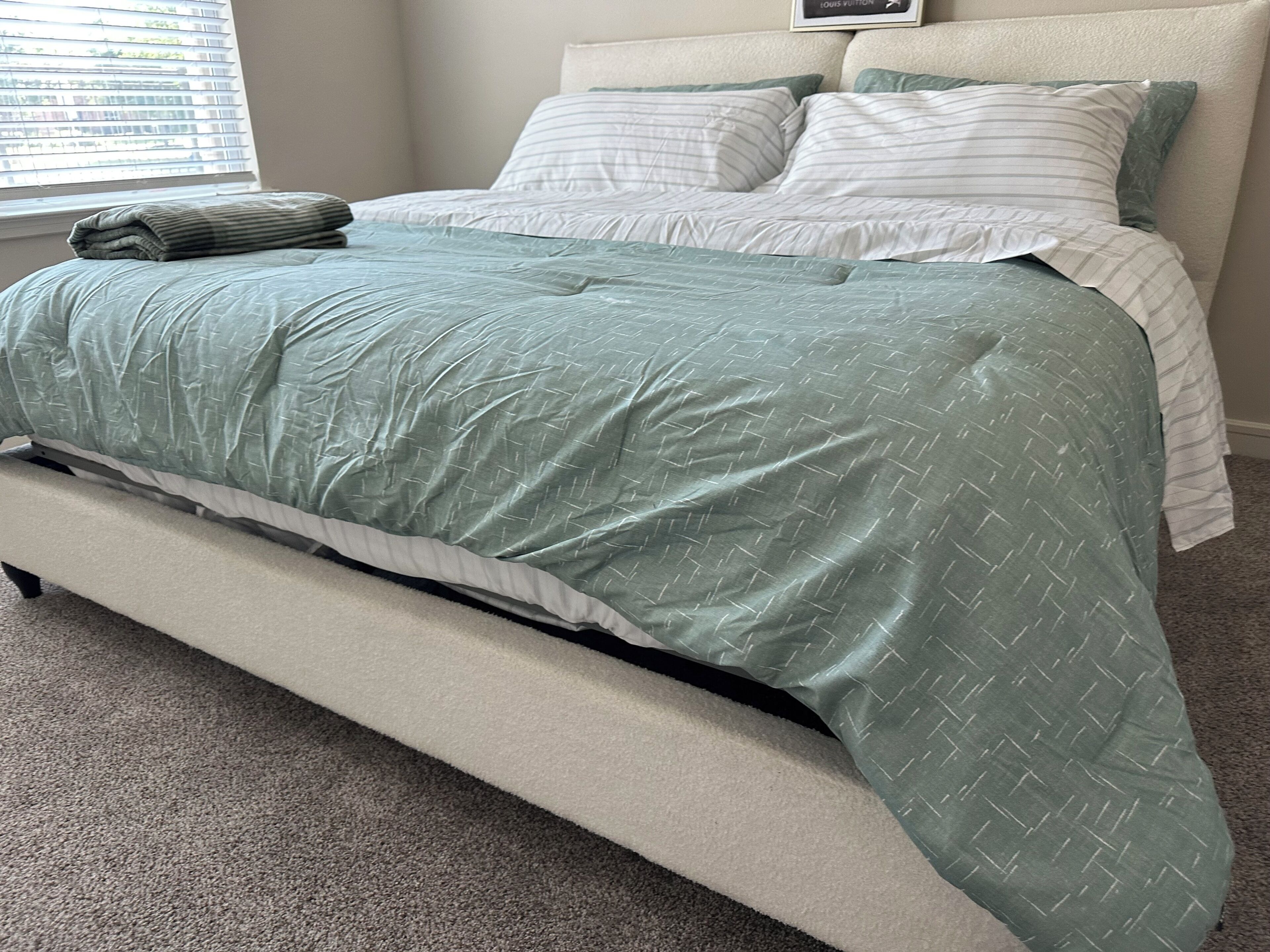 A bed with a green quilt, a white pillow, and a grey pillow.