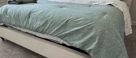 Una cama con un edredón verde, una almohada blanca y una almohada gris.