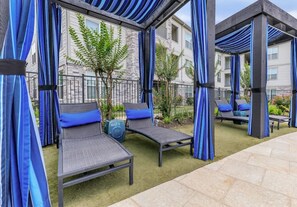 An outdoor seating area with cushioned chairs and a small table, surrounded by blue curtains and a stone building in the background. - 2-bedroom 2-full bath apartment in adorable Houston Energy Corrido area (Houston)