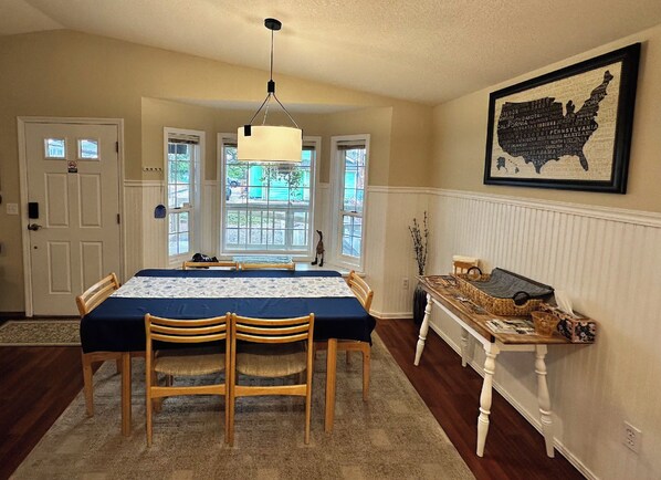 A dining room with a table set for four, a chandelier, a view through the windows, and a map of the United States on the wall.