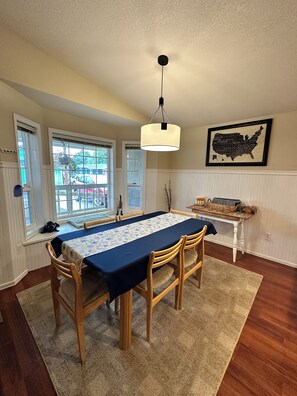 A dining area with a table set for four, wooden chairs, a hanging light fixture, and a map of the USA on the wall.