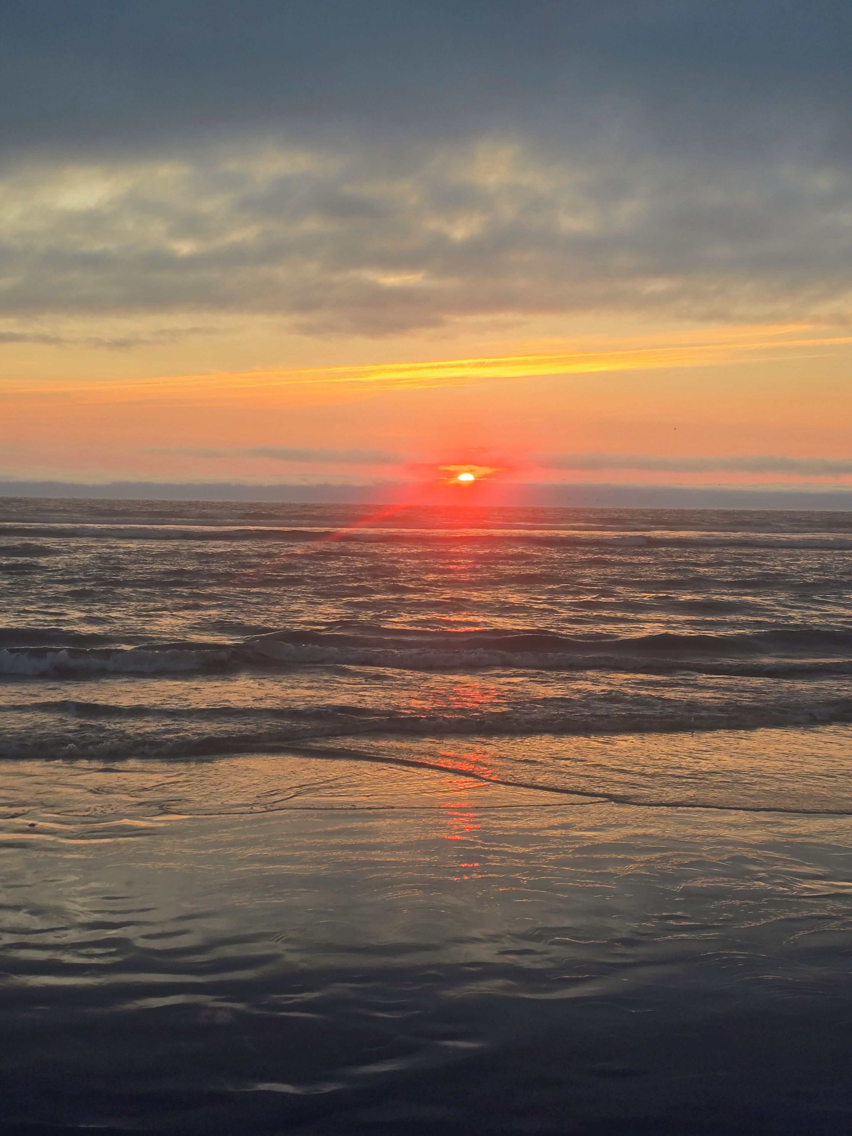 Un coucher de soleil sur l’océan, les vagues reflétant les couleurs du ciel.