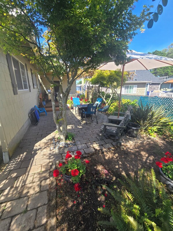 A patio area with a table and chairs, a potted plant, and a small garden with red flowers.