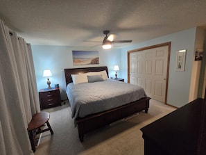 A bedroom with a bed, bedside tables, a ceiling fan, a door, and a small stool.