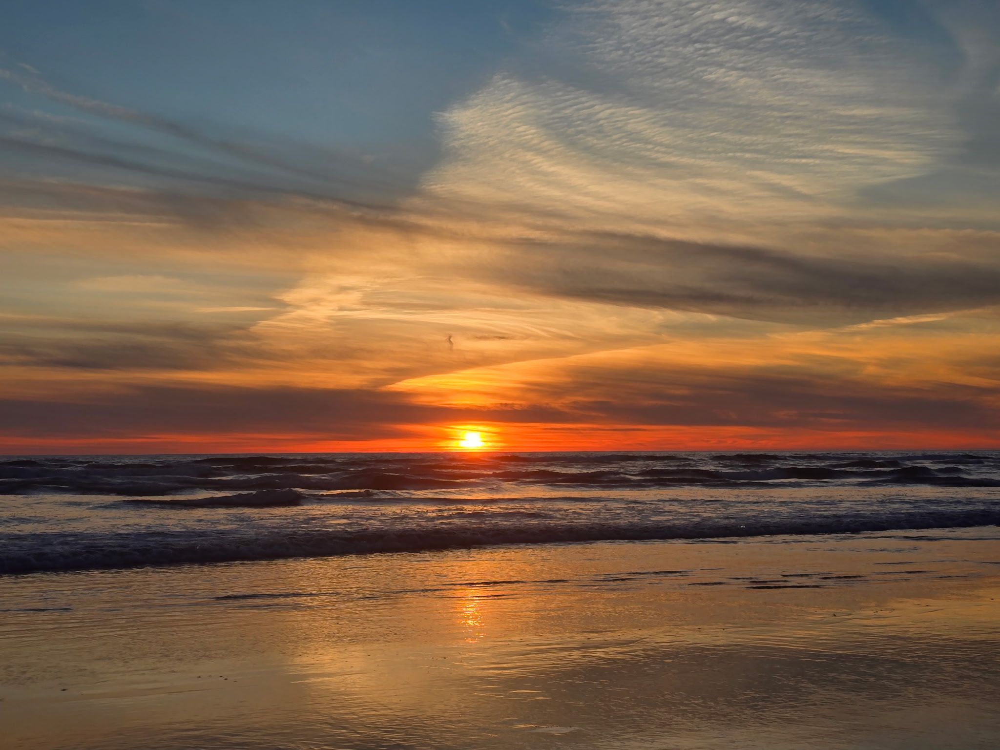 A beach with waves and a sunset.