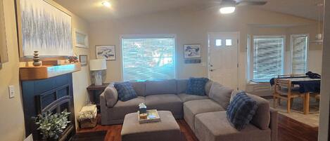 A living room with a sectional sofa, a fireplace, a dining area, and a ceiling fan.
