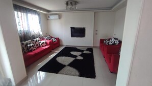 A living room with two red sofas, a black and white patterned rug, and a flat-screen TV mounted on the wall. - Luxrious Comfy Apartments East Cairo (Cairo Governorate)