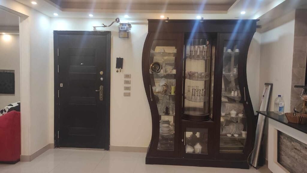 A room with a black door, a glass-fronted cabinet with dishes, and a red chair.