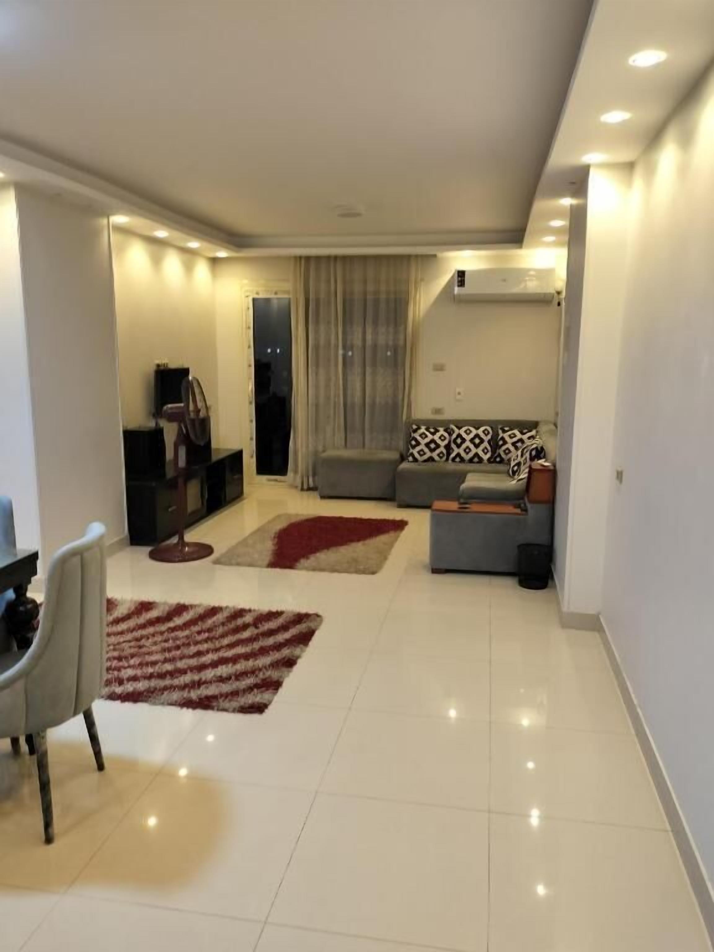 A modern living room with a sofa, a coffee table, a TV, and a dining area with chairs.