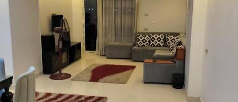 A modern living room with a sofa, a coffee table, a TV, and a dining area with chairs.