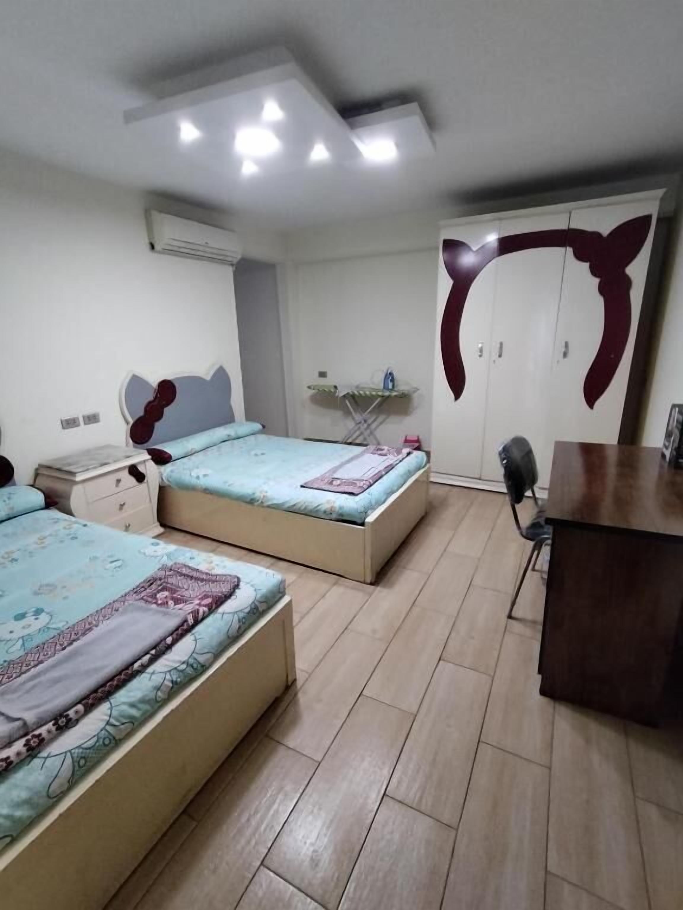 A bedroom with two beds, a desk, and a wardrobe.