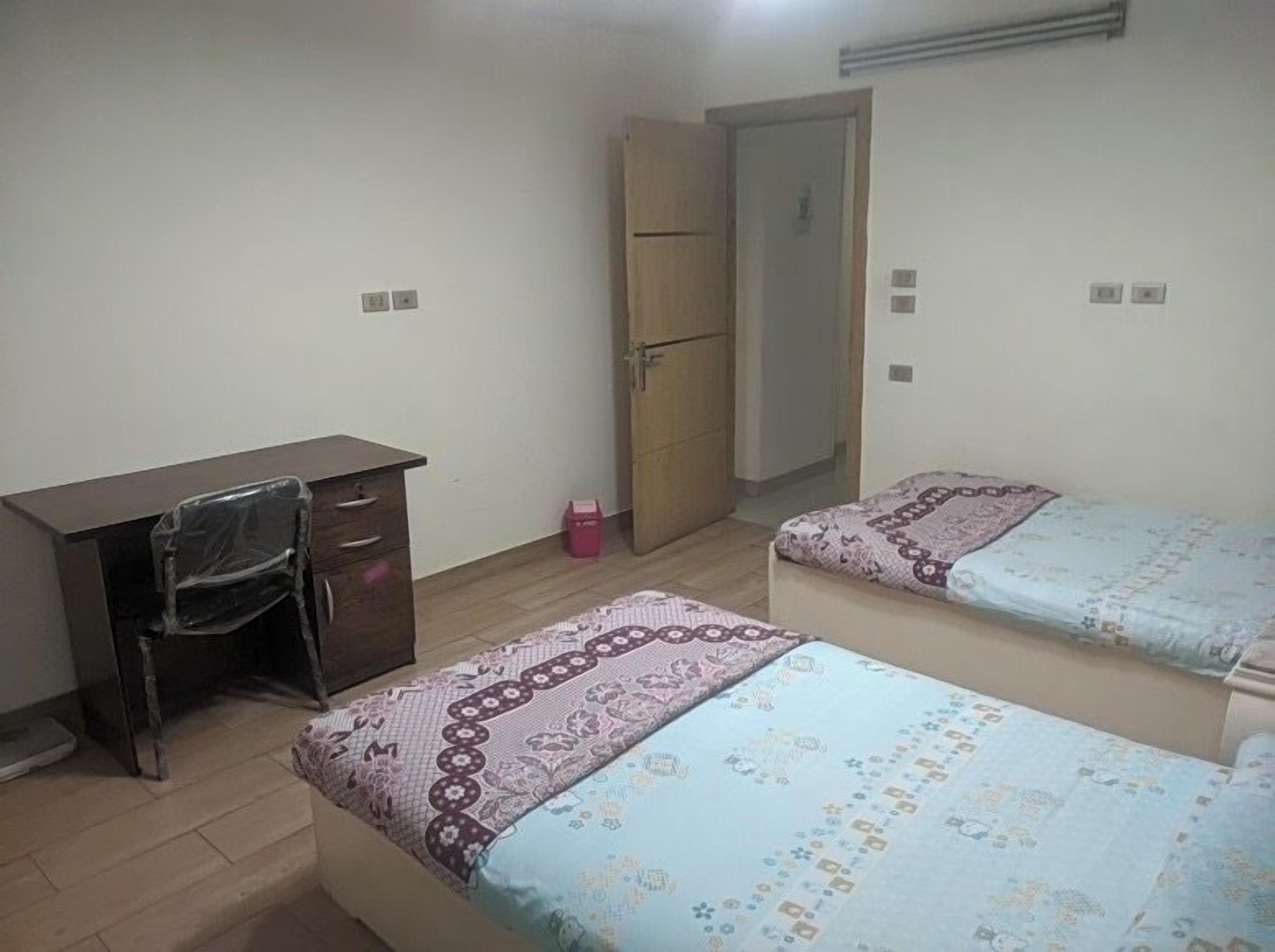 A room with a desk, two beds, a wardrobe, and a door.