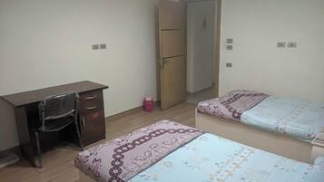 A room with a desk, two beds, a wardrobe, and a door.