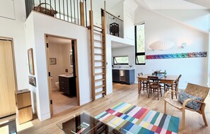 Un espai de menjador ample amb un sostre alt, una escala, una cuina i una zona de dinar amb un farrató de colors.