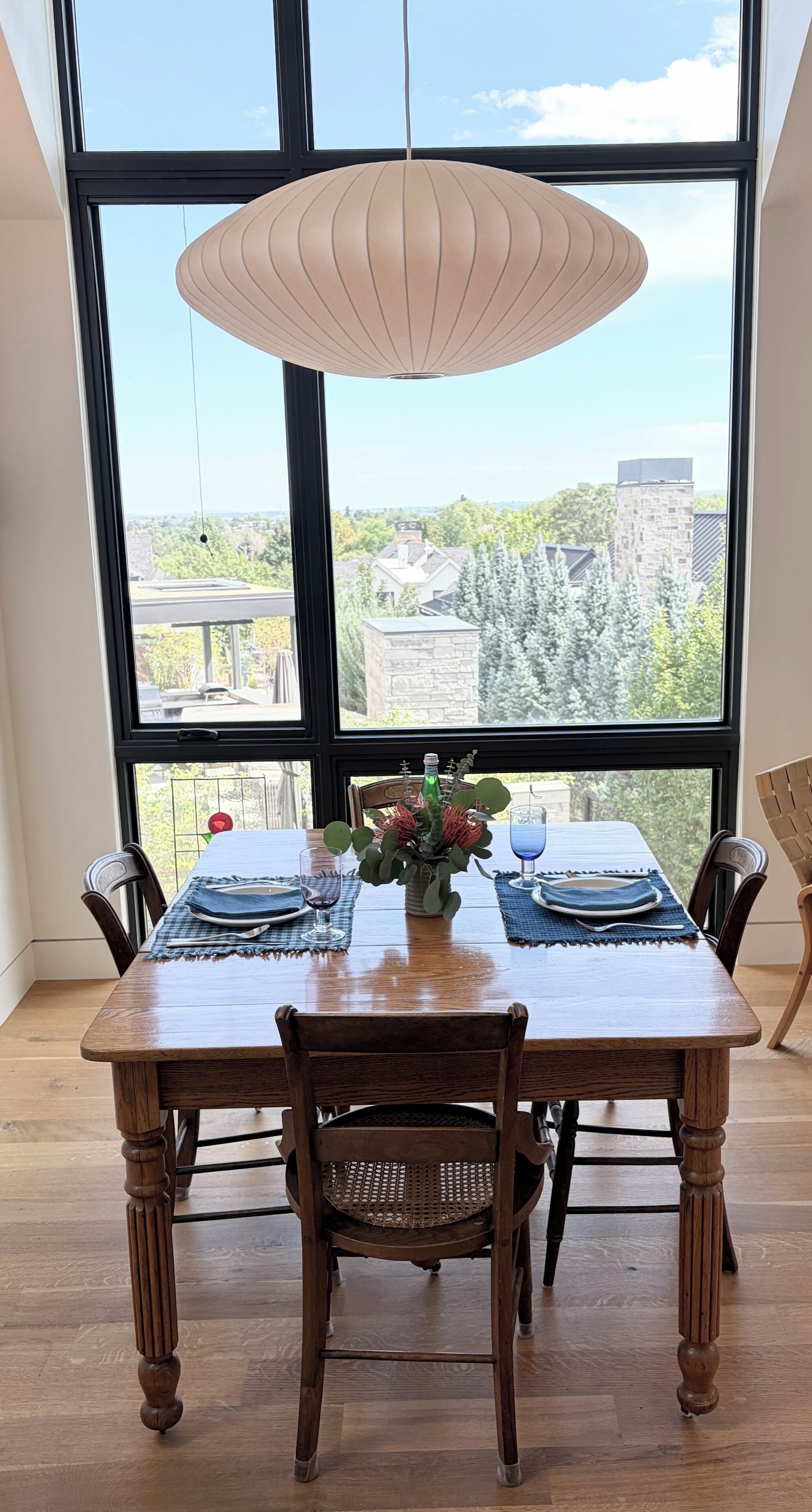 Une table à manger dressée avec des sets de table, un vase rempli de fleurs et un luminaire suspendu.