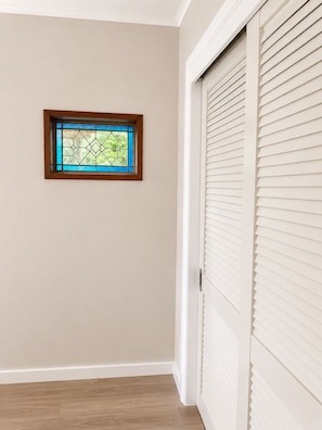 A room with a wooden-framed stained glass window, a white door with blinds, and a wooden floor.