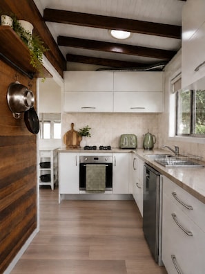 A modern kitchen with white cabinets, stainless steel appliances, and a wooden accent wall.