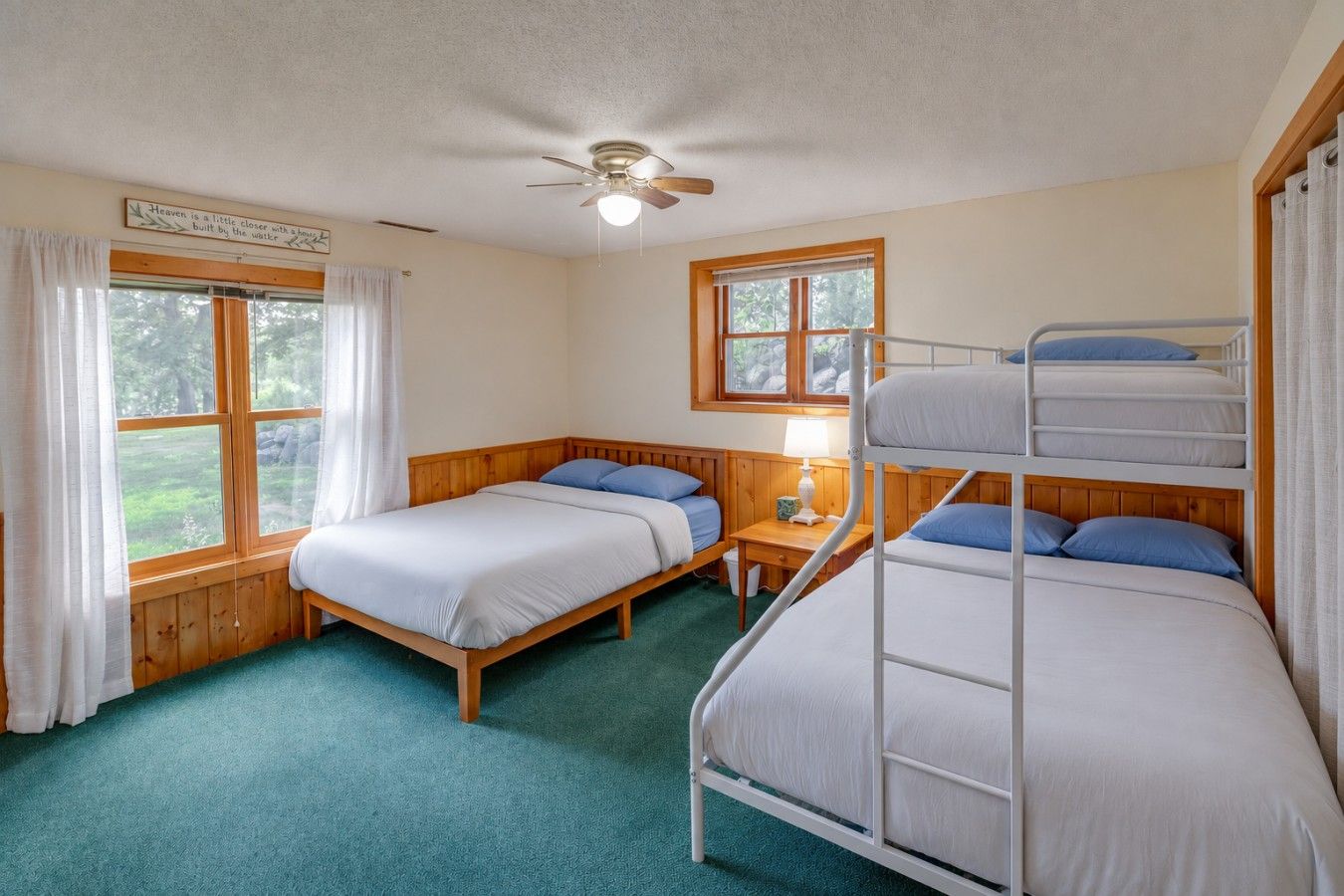 A room with bunk beds, a ceiling fan, a window with curtains, and a bed with a wooden headboard.