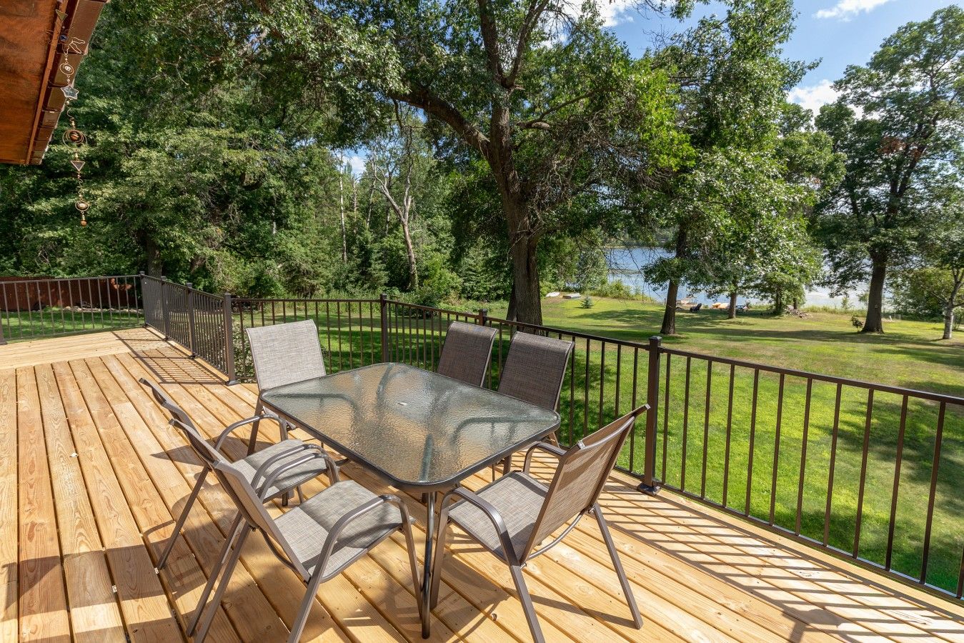 Eine Terrasse mit Tisch und Stühlen mit Glasplatte, umgeben von einem Metallgeländer, mit Blick auf eine grüne Fläche mit Bäumen.