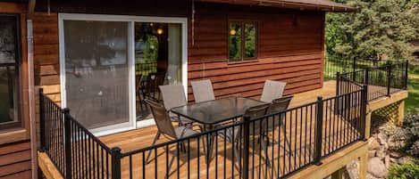 Una cabaña de madera con terraza, una puerta de cristal que da a un patio y una mesa con sillas.