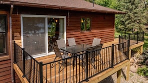 A wooden cabin with a deck, a glass door leading to a patio, and a table with chairs.