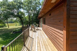 A wooden deck with a railing, a table, and chairs, overlooking a grassy area with trees. - Blue Flag Shores Private Home (Pequot Lakes)