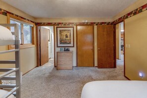 A bedroom with a bunk bed, a dresser, a framed picture, and a door leading to another room.