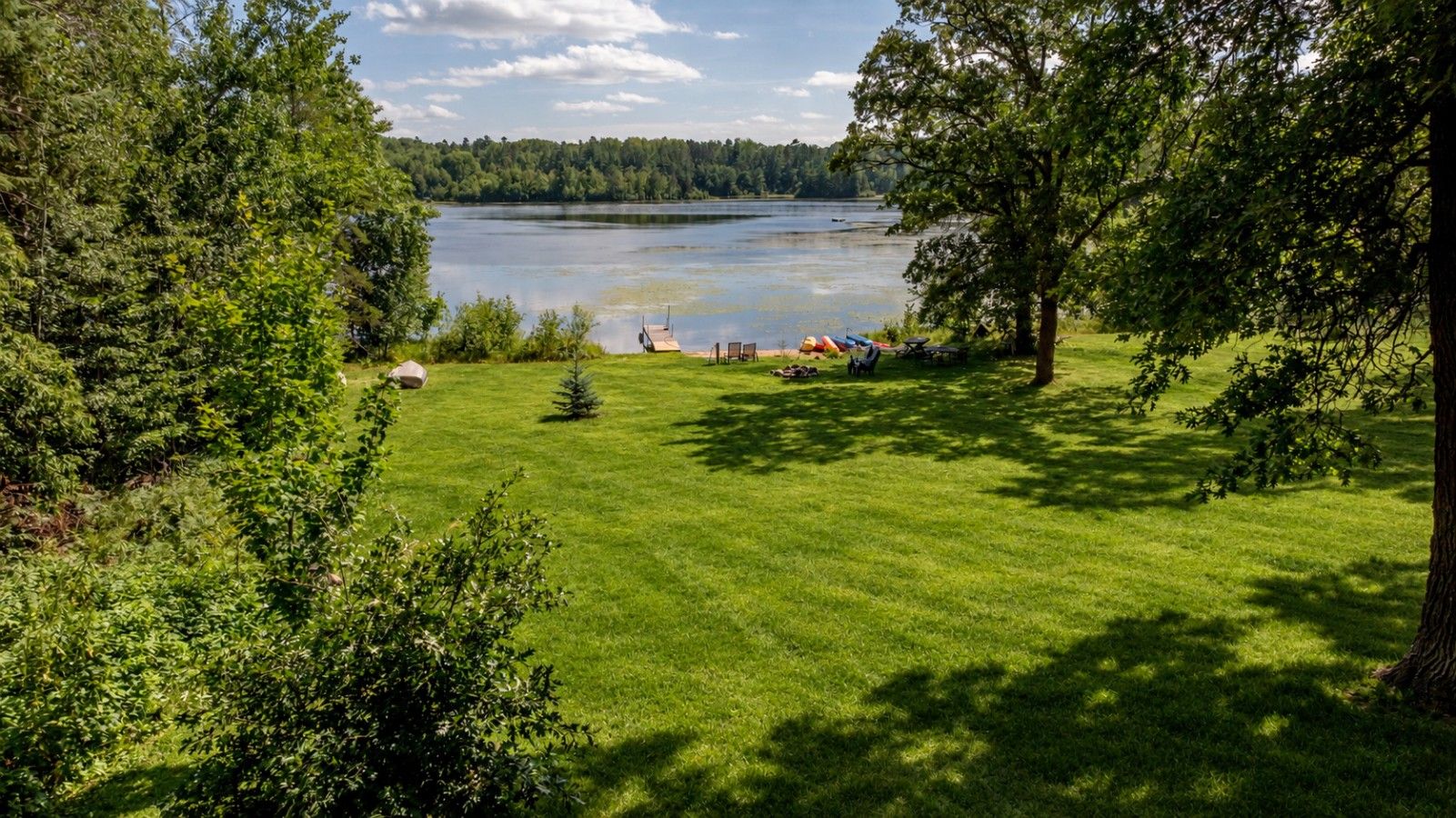 A grassy area with a lake, trees, and a dock.