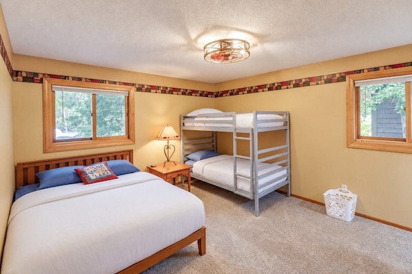 A bedroom with a single bed, a bunk bed, a nightstand, a lamp, and a window.