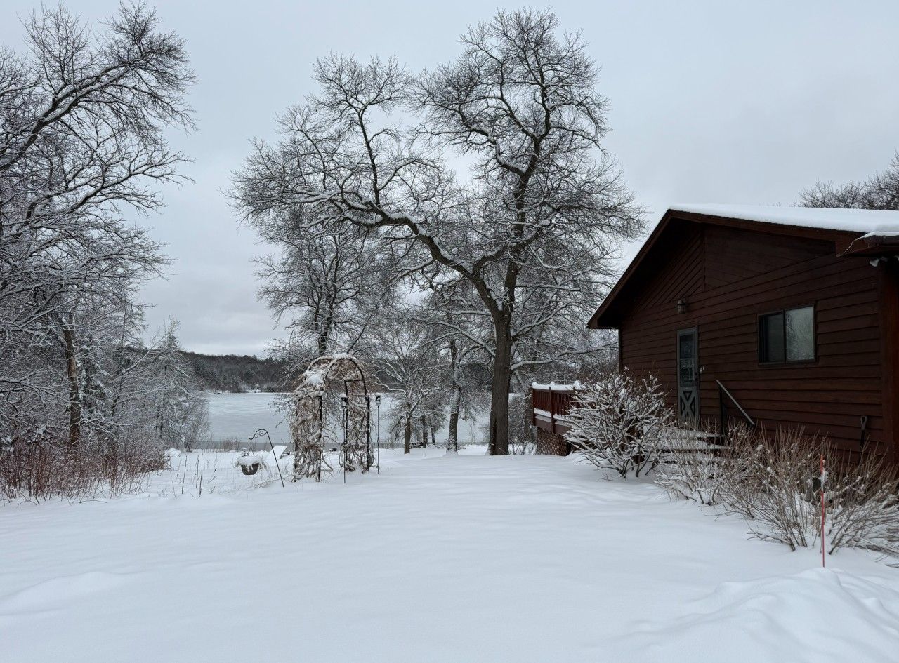 A snow-covered landscape with a wooden cabin and leafless trees.