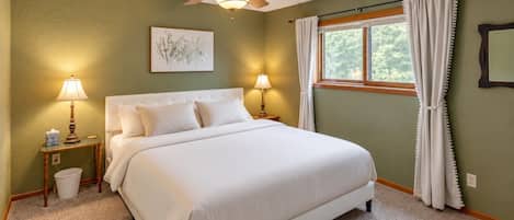 A bedroom with a bed, two bedside tables, a ceiling fan, a window with curtains, and a framed picture on the wall.