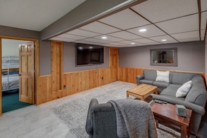 A room with a grey sofa, wooden panel walls, a flat-screen TV, and a wooden coffee table.