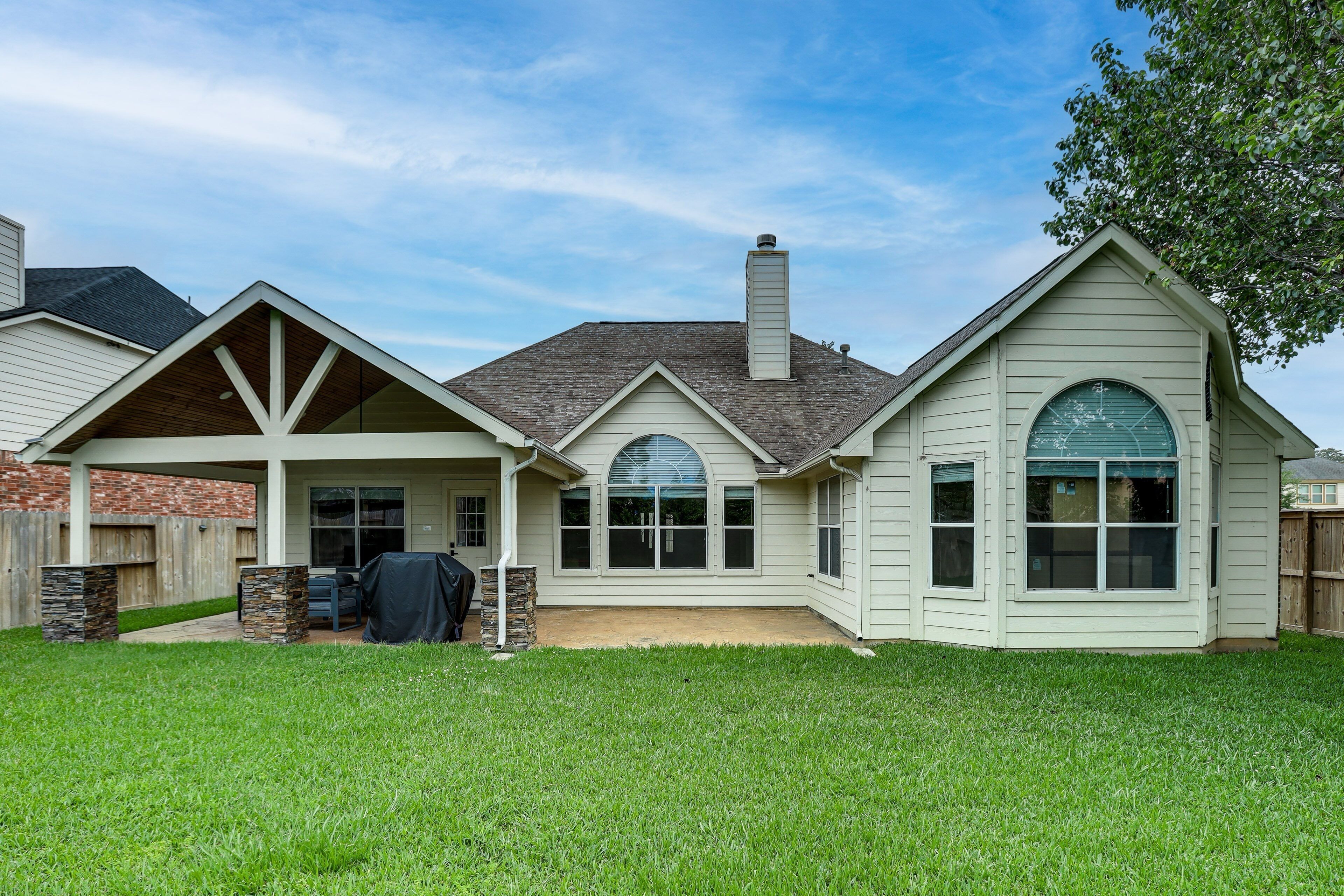 A residential house with a covered patio, a chimney, and a stone accent wall.