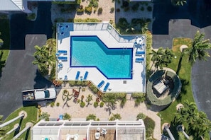 Eine Vogelperspektive auf ein Hotel mit Schwimmbad, Liegestühlen und Palmen.