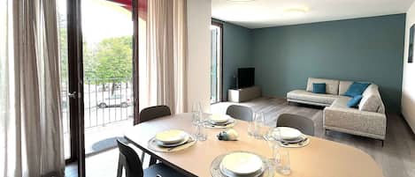 Uma sala de estar moderna com área de jantar, mesa posta para quatro pessoas, sofá e televisão.