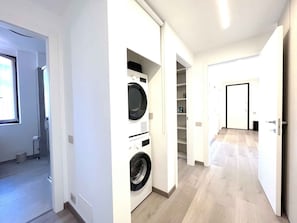 A laundry room with a washing machine and dryer, a hallway with a door at the end, and a window providing natural light. - Holiday flat with balcony (Angera)