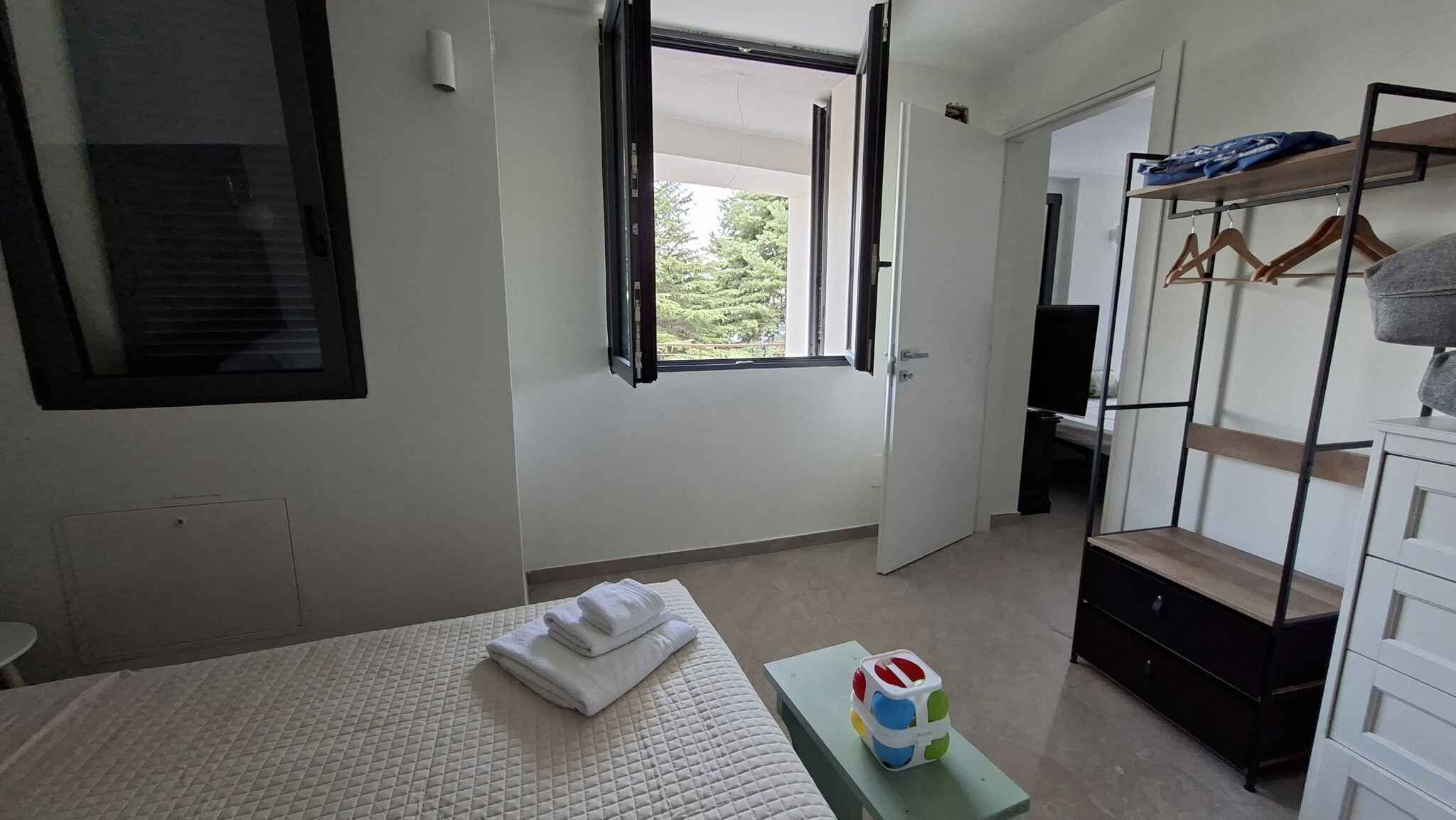 Une chambre d’hôtel avec un lit, une petite table sur laquelle se trouve un jouet, une armoire et une fenêtre donnant sur un paysage verdoyant.
