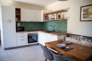 A compact kitchen with white cabinets, a microwave, an oven, and a sink. There's a dining table with plates and glasses. - Holiday flat with terrace (Lesa)