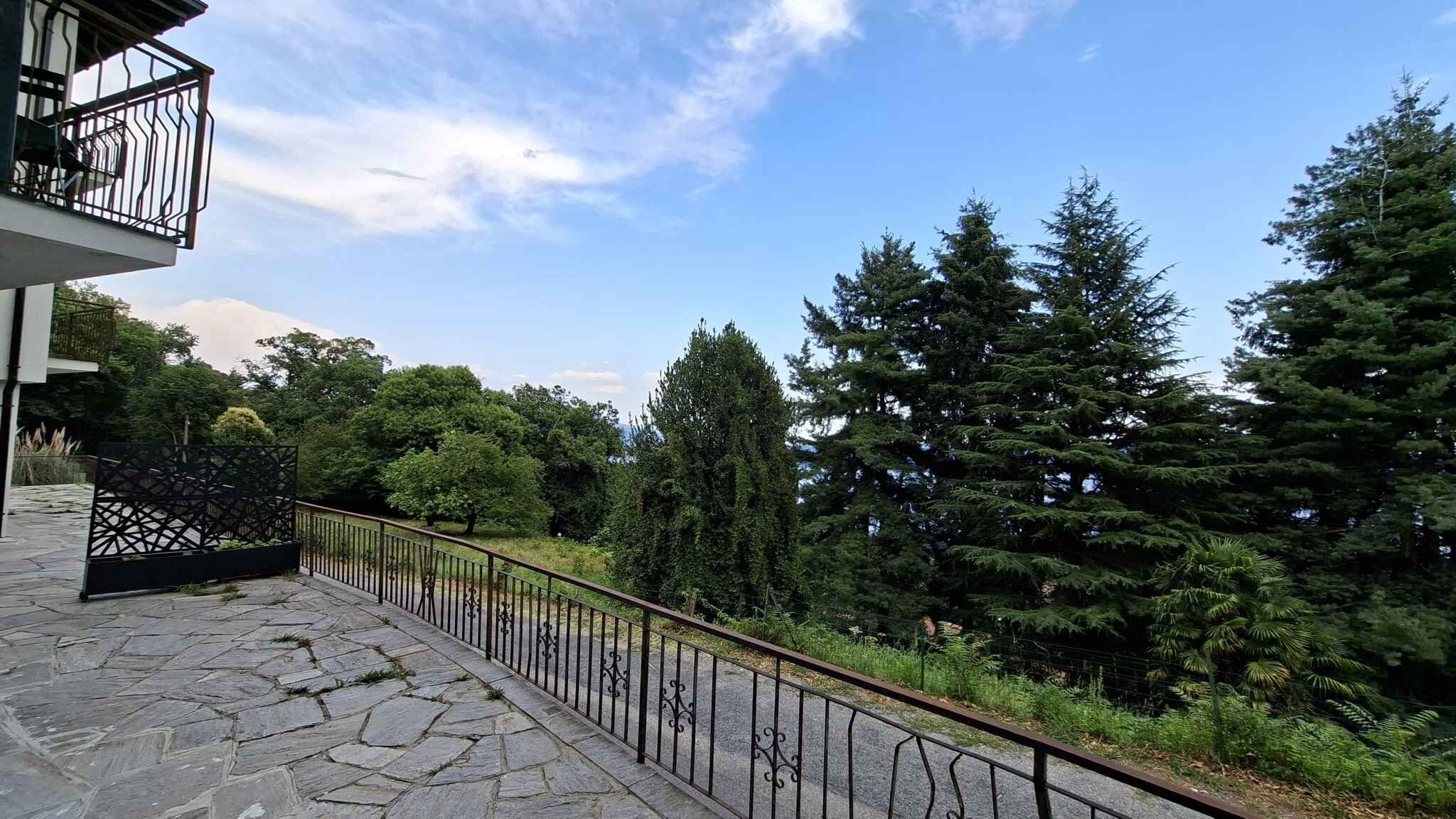 Un balcon dallé de pierres, avec une balustrade en métal, donnant sur une zone boisée.