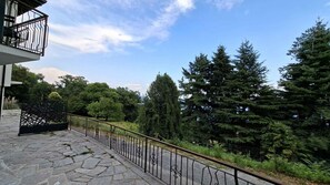 A stone-paved balcony with a metal railing overlooking a forested area. - Holiday flat with terrace (Lesa)
