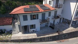 A multi-story building with a red-tiled roof, solar panels, and a courtyard with outdoor furniture. - Holiday flat with terrace (Lesa)