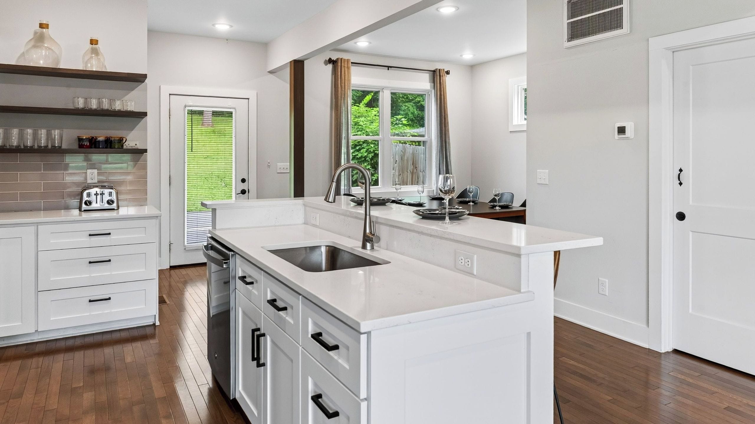 Una cocina moderna con armarios blancos, un lavamanos de acero inoxidable y una ventana con cortinas.