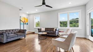 Ein geräumiges Wohnzimmer mit großem Fenster, Deckenventilator und Holzboden.