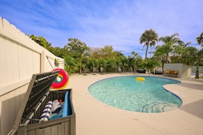Ein Swimmingpool mit klarem Wasser, umgeben von einer Sandterrasse und Palmen.