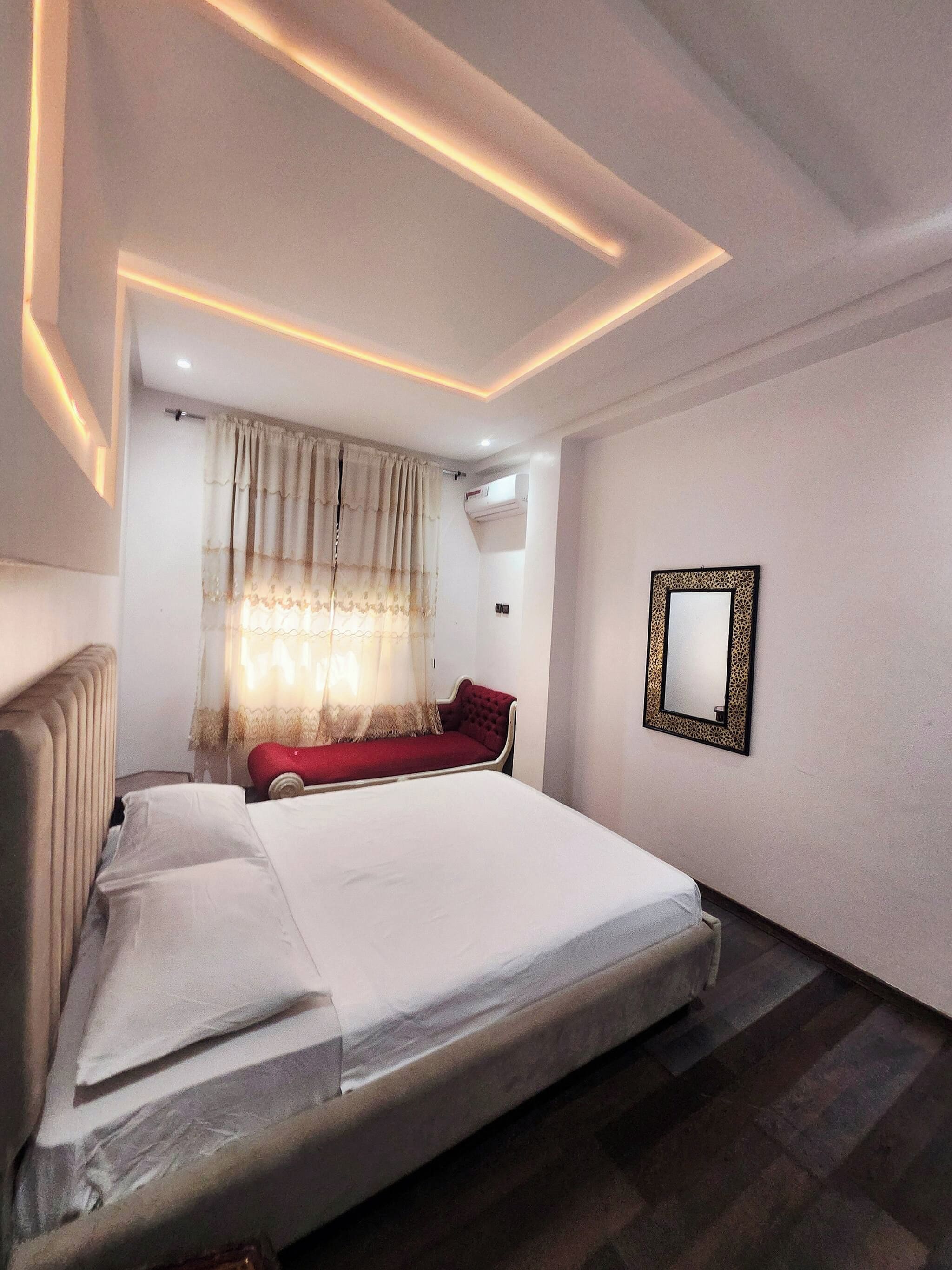 Un dormitorio con una cama, un sofá rojo, un espejo y una lámpara en el techo.