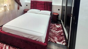 Een moderne slaapkamer met een groot bed, een kledingkast, een spiegel en decoratieve plafondpanelen.