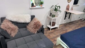 Una sala de estar moderna con un sofá gris, almohadones mullidos, una pequeña mesita auxiliar blanca y una cama azul.